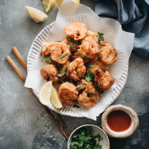 Fried shrimp served in plate with parchment paper with chopped cilantro and sauce on the side