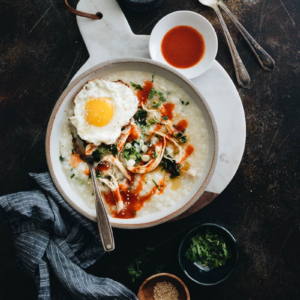 Instant Pot congee with chicken and spinach topped with egg served in a bowl with sauce and toppings on the side
