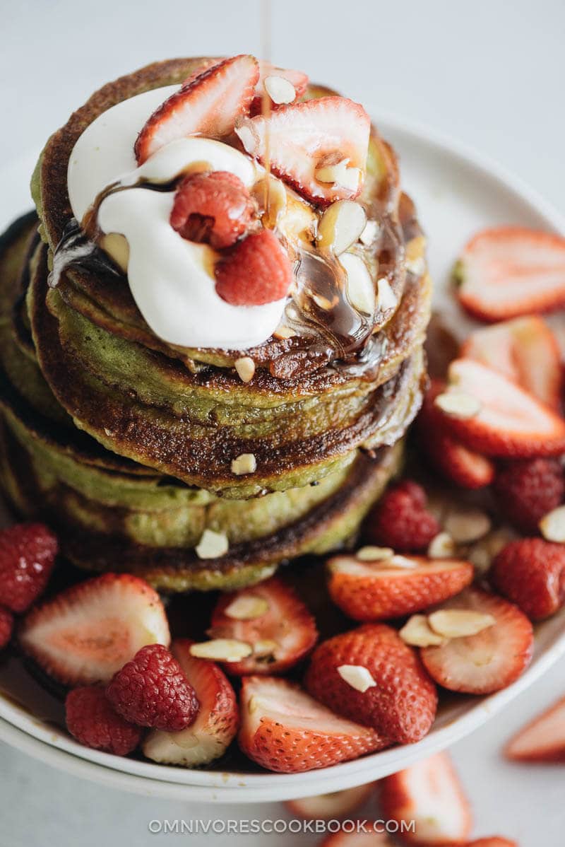 Super close up of a stack matcha pancakes with strawberry topping and whipped cream