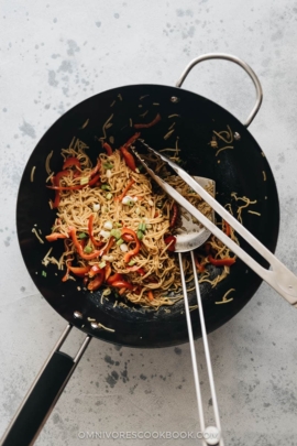 Garlic noodles cooked in a wok with spatula and a pair of tongs