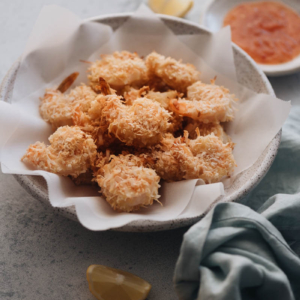 A bowl of crispy coconut shrimp served with sweet chili sauce and lemon