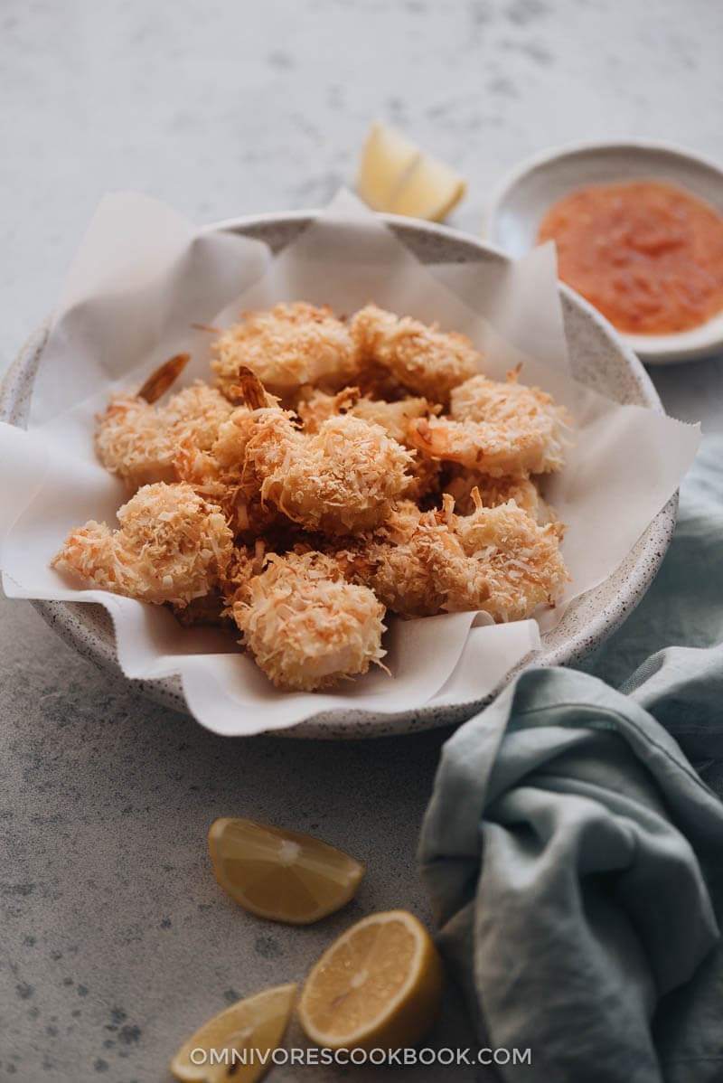 A bowl of crispy coconut shrimp served with sweet chili sauce and lemon