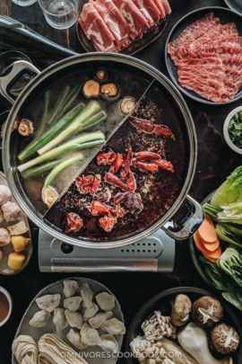 Close up of Chinese hot pot with two types of broth and ingredients on the side