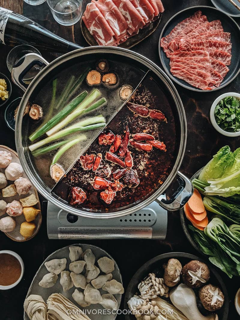 Close up of Chinese hot pot with two types of broth and ingredients on the side