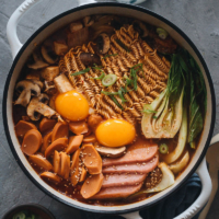 Korean Army Stew (Budae Jjigae) - Rich spicy broth made with aromatics, ground meat, and noodles, topped with sausage, veggies and runny egg yolks. An easy one-pot meal that requires very little prep and is fast to make.