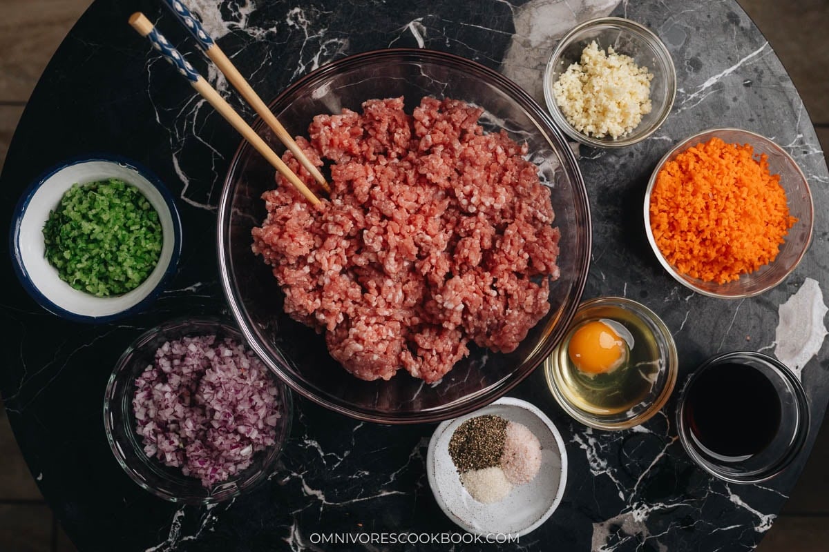 Lumpia Shanghai ingredients laid out in bowls on a dark table.