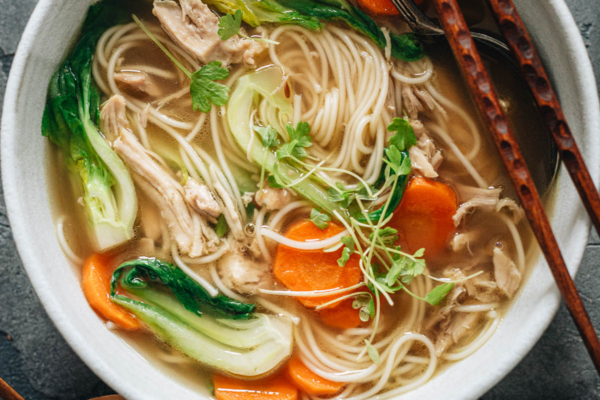 Bowl of noodle soup with shredded chicken, carrot and baby bok choy