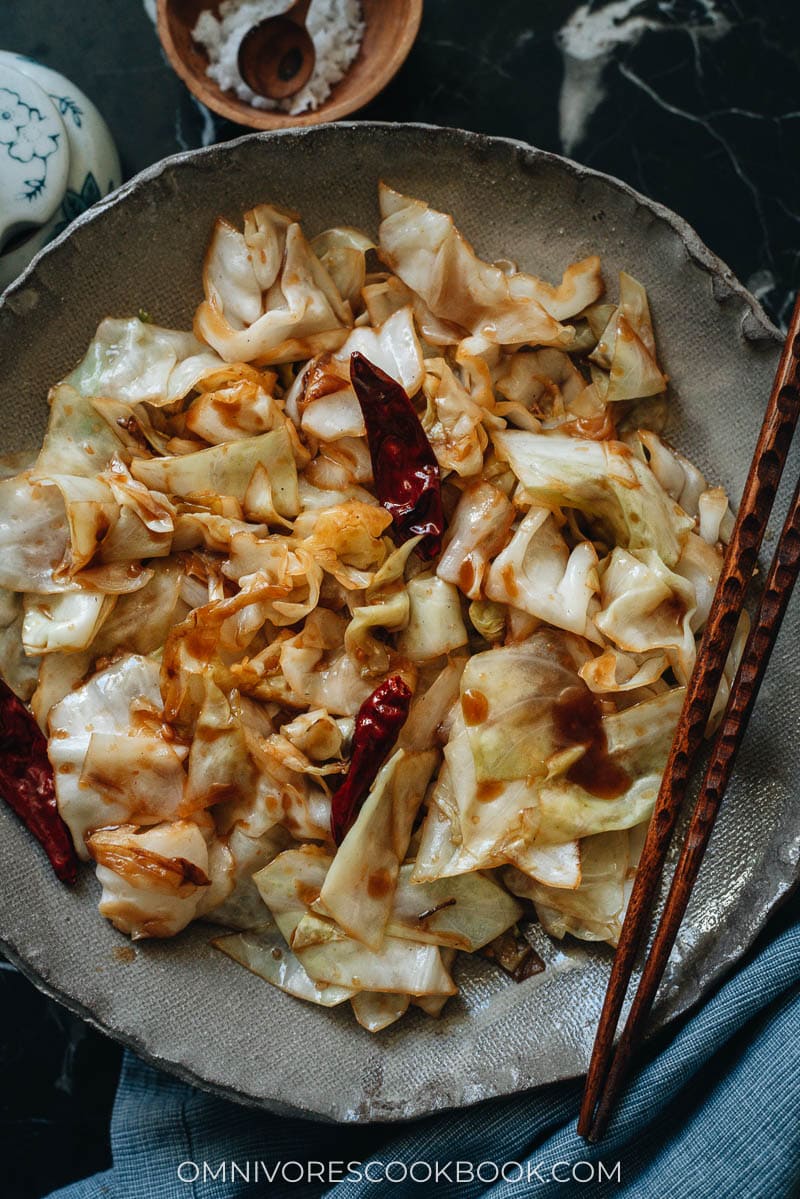 A bowl of sauteed cabbage with chile peppers and chopsticks