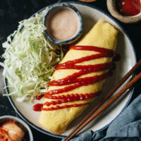 Kimchi Omurice is some next-level comfort food: umami kimchi fried rice is wrapped cozily into a creamy scrambled egg omelet, topped with a drizzle of ketchup.