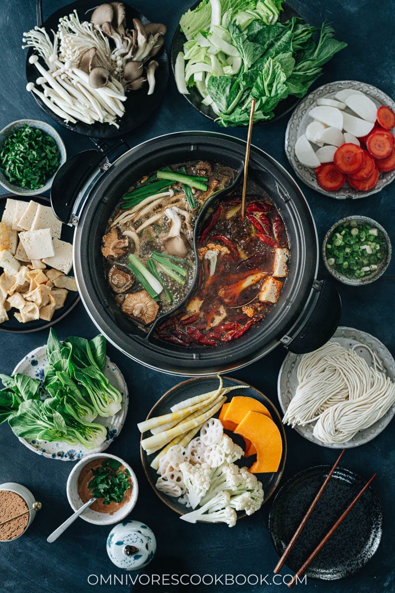Hot pot with a divider serving spicy and non-spicy broth with vegetables on the side