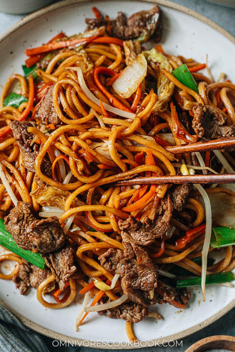 Closeup of chopsticks grabbing a bite of beef lo mein