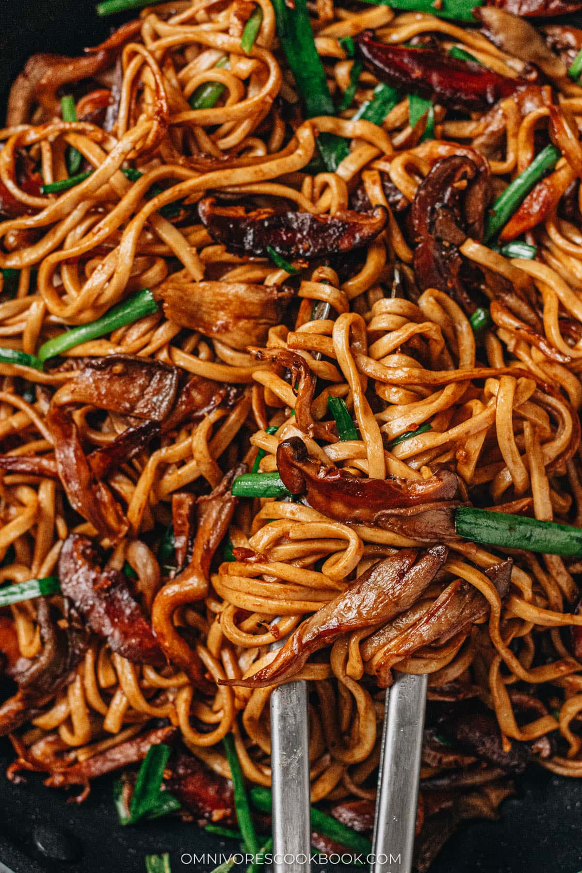 Tossing mushroom longevity noodles in a pan close up