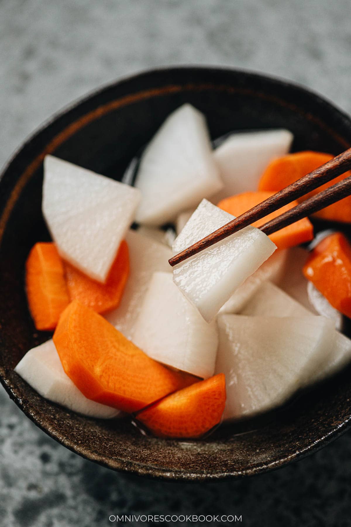 Close up shot of pickled daikon pickled up with a pair of chopsticks