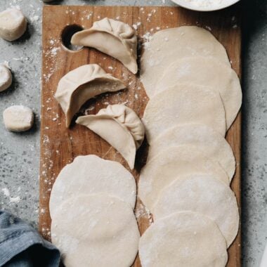 Homemade dumpling wrappers and uncooked dumplings on a cutting board