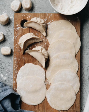 Homemade dumpling wrappers and uncooked dumplings on a cutting board