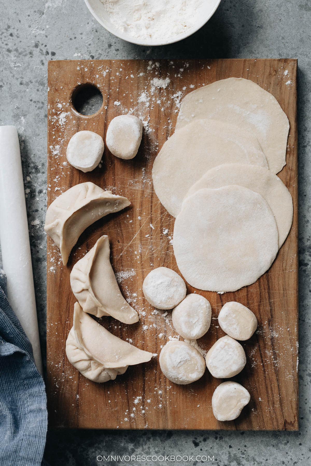 Homemade dumpling wrappers and uncooked dumplings on a cutting board with rolling pin