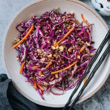 Crisp Chinese coleslaw with purple cabbage, carrots, peanuts, and cilantro in a ceramic bowl with chopsticks.