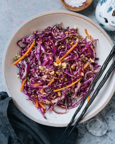 Crisp Chinese coleslaw with purple cabbage, carrots, peanuts, and cilantro in a ceramic bowl with chopsticks.