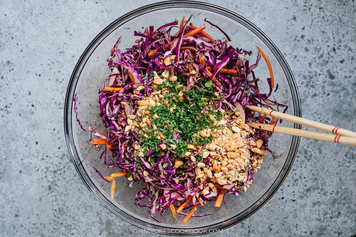 Tossing Chinese coleslaw with chopsticks, mixing cabbage, carrots, cilantro, and crushed peanuts.