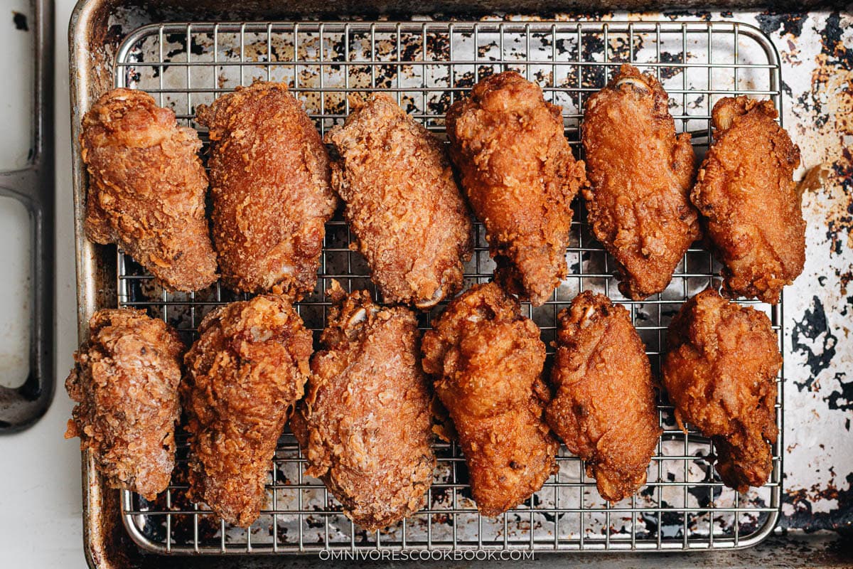 Freshly fried chicken wings resting on a wire rack over a baking sheet to drain excess oil after double frying.