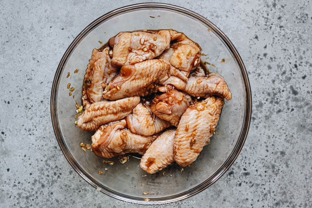 Chicken wings mixed with soy sauce, oyster sauce, garlic, and scallion in a glass bowl, showing the marinating step.
