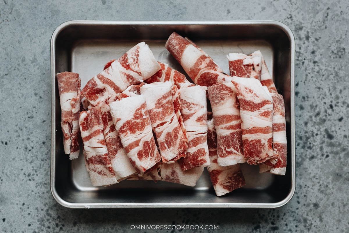 Tray of frozen thinly sliced beef rolls arranged neatly.
