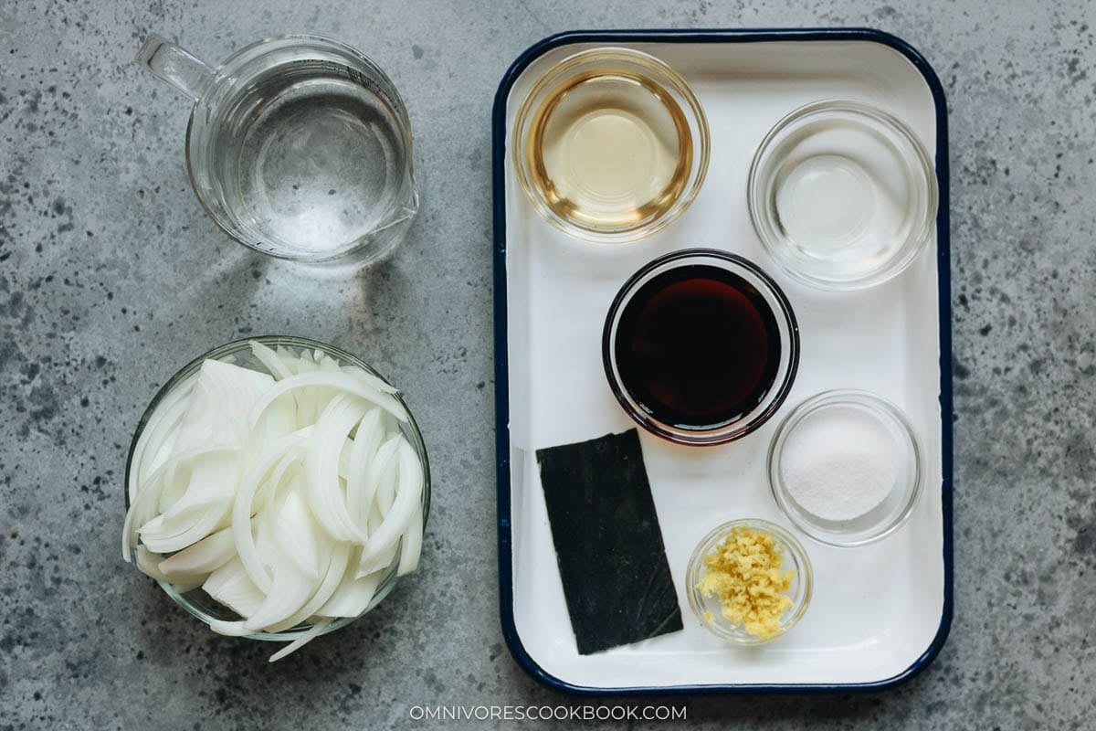 Gyudon ingredients arranged on a gray countertop, including sliced onions, soy sauce, mirin, sake, kombu, sugar, ginger, and water in small bowls.