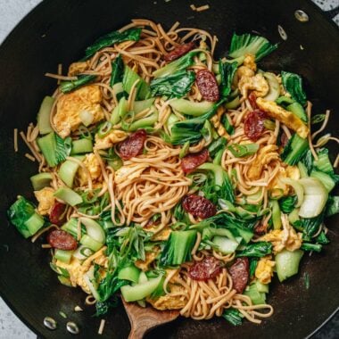 Wok of Chinese fried noodles with baby bok choy, scrambled eggs, and Chinese sausage.