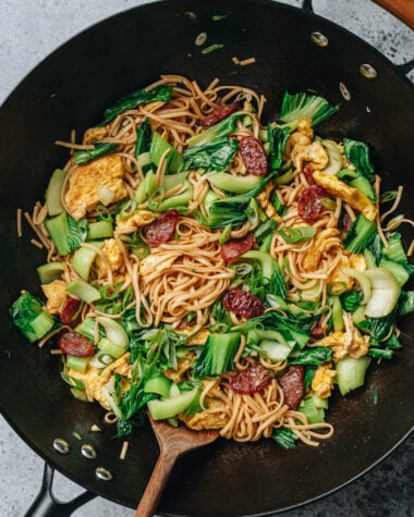 Wok of Chinese fried noodles with baby bok choy, scrambled eggs, and Chinese sausage.