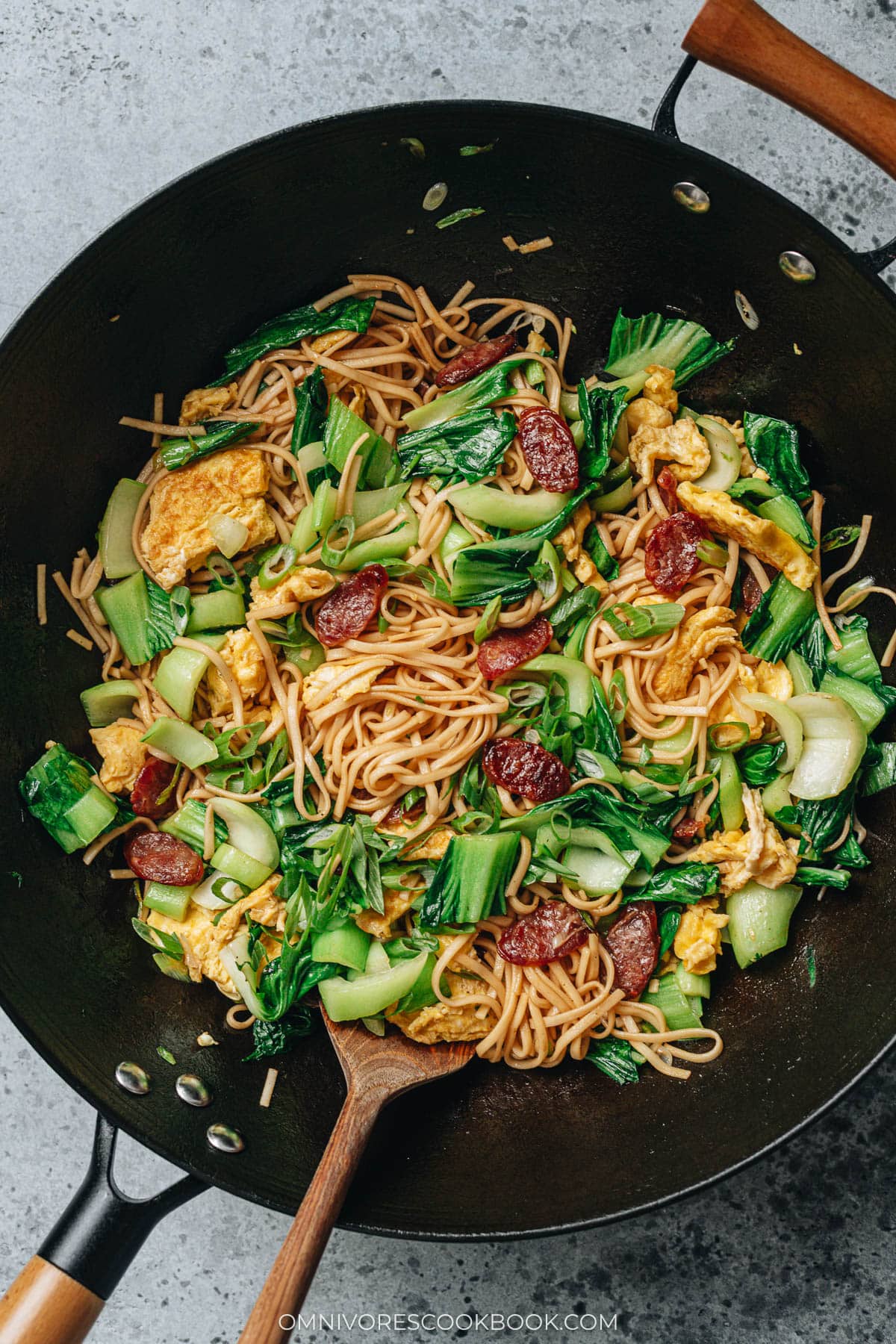 Wok of Chinese fried noodles with baby bok choy, scrambled eggs, and Chinese sausage.