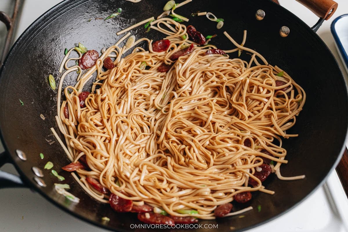 Noodles added to the wok with sausage and scallions, covered with sauce.