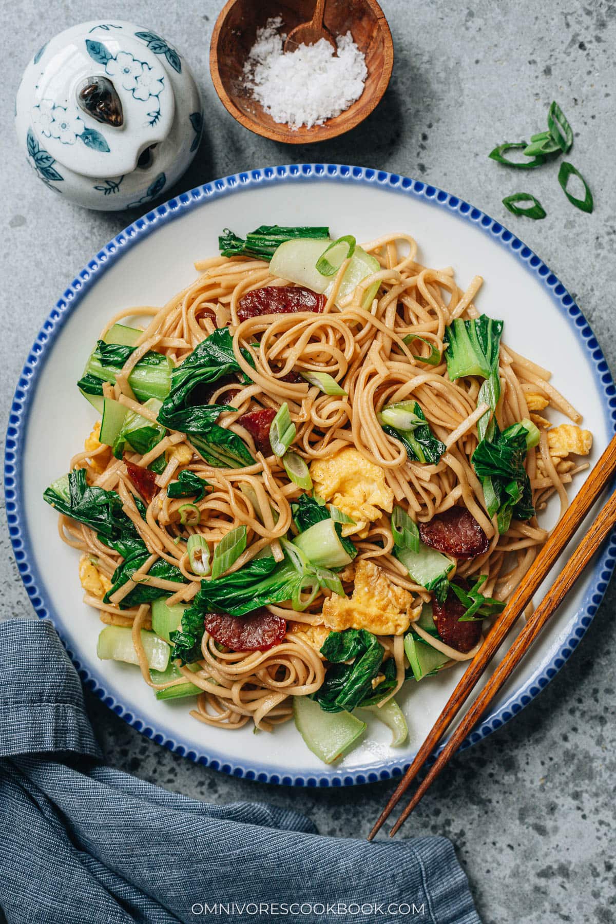 Plate of Chinese fried noodles with bok choy, sausage, and eggs, served with chopsticks for an easy weeknight meal.