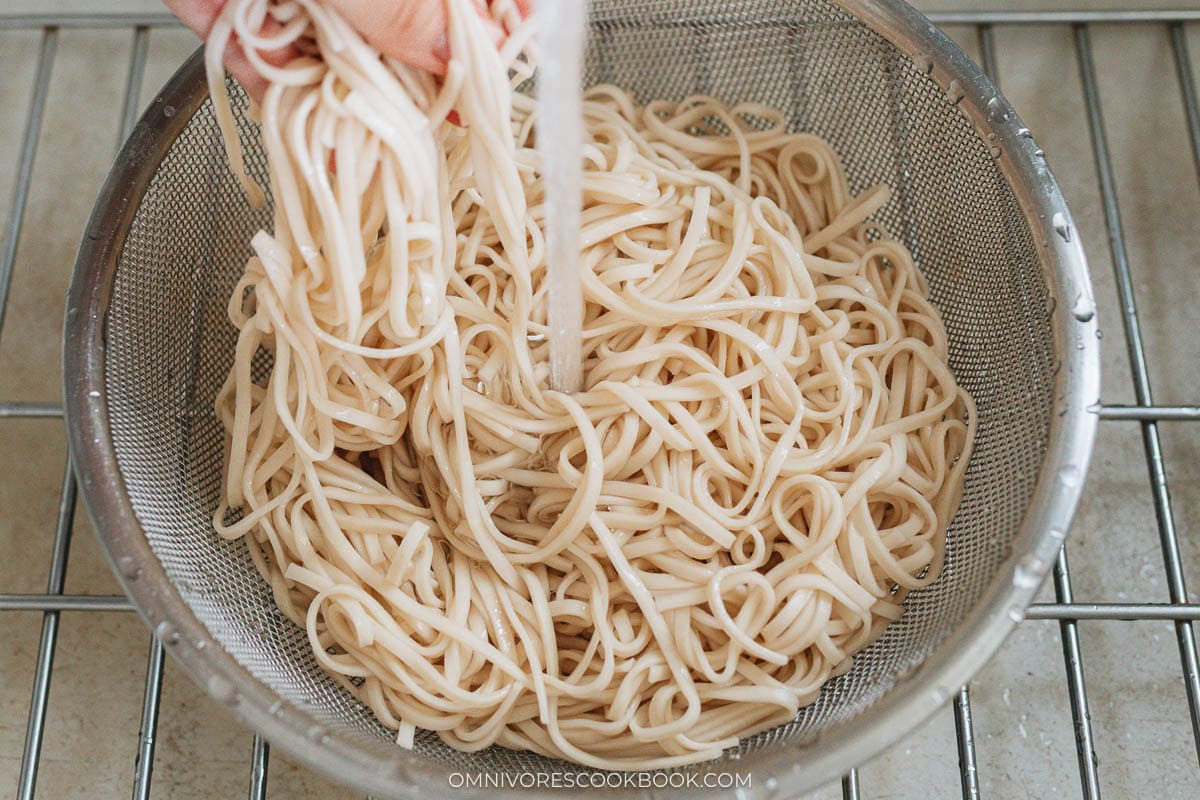 Cooked wheat noodles being rinsed in cold water to stop cooking.