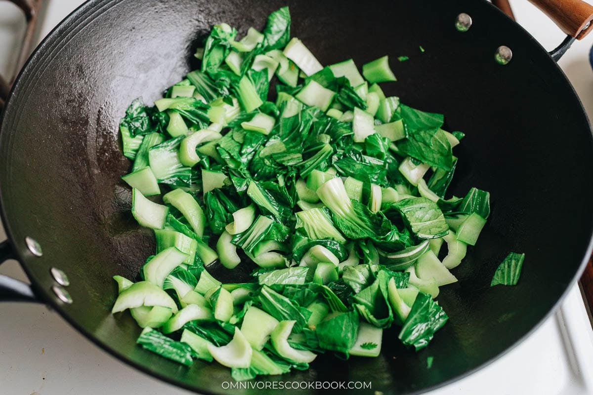 Freshly chopped baby bok choy stir frying in a wok.