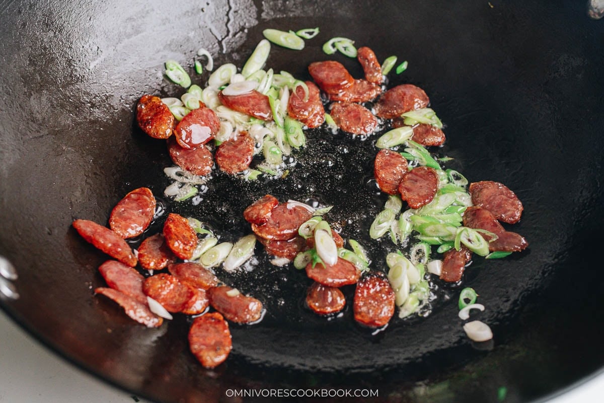 Sliced Chinese sausage and scallions sizzling in oil in a wok.