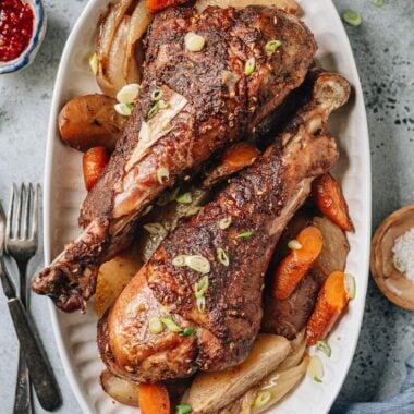 Roast turkey legs over a bed of vegetable served in a platter