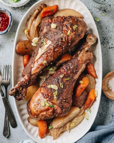 Roast turkey legs over a bed of vegetable served in a platter