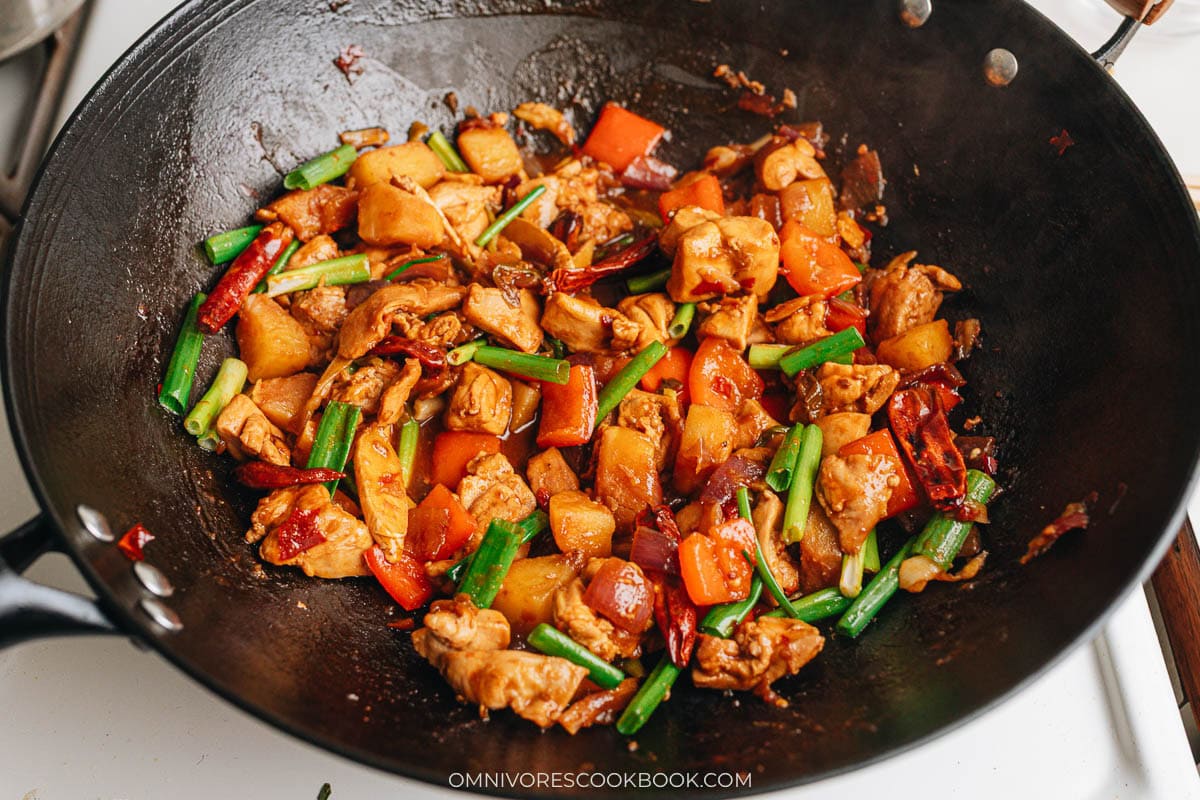 Final simmer stage showing chicken, potatoes, peppers, and scallions coated in reduced sauce in the wok.
