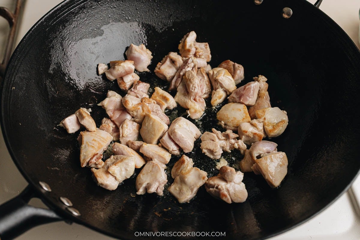 Chicken pieces searing in a wok until lightly golden on the edges.