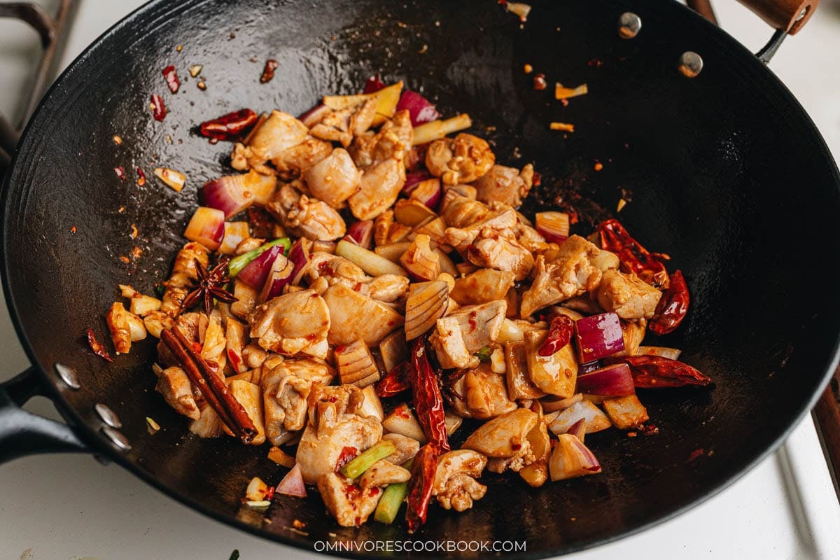 Aromatics, dried chilis, and chicken stir-frying together in the wok after adding doubanjiang.