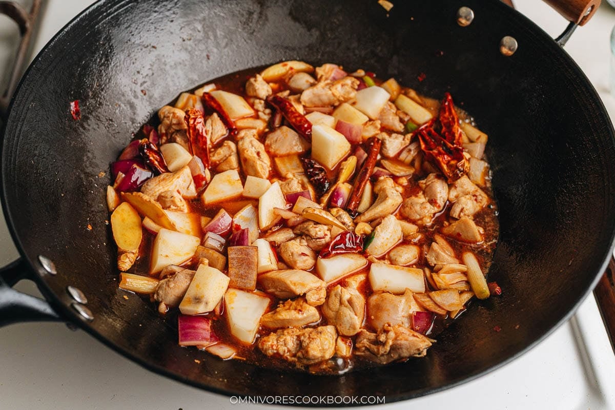 Chicken and potatoes simmering in broth with spices and red onions in the wok.