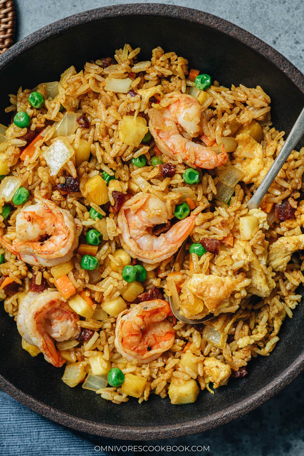 Top-down view of pineapple fried rice in a bowl, with shrimp and peas visible throughout the rice.