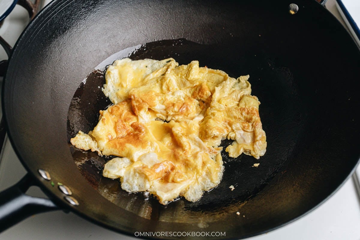 Eggs cooking in a wok, forming a soft omelet before being scrambled.