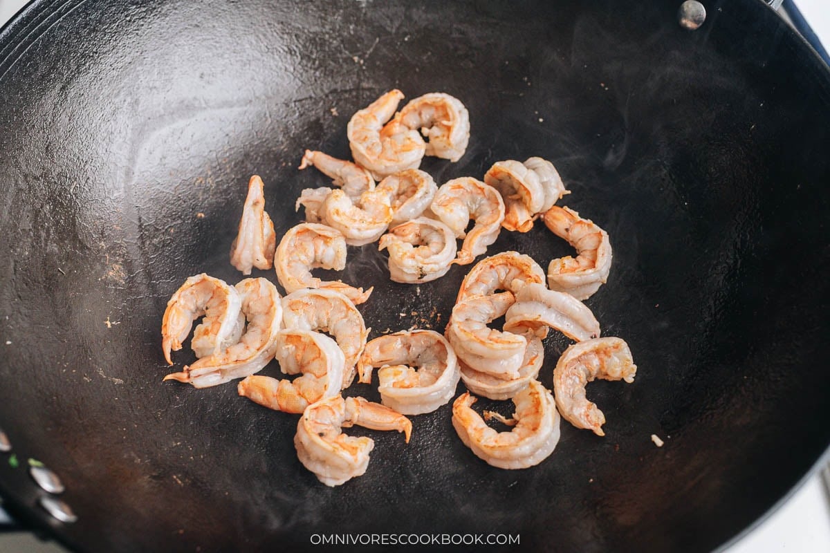 Shrimp searing in a hot wok until just cooked and pink.