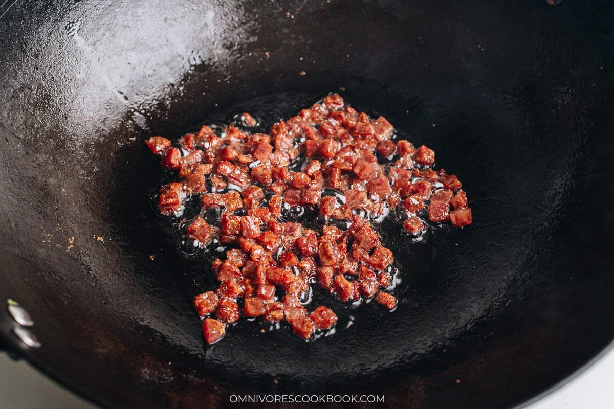 Diced lap cheung frying in oil in a wok until slightly crisp and browned.