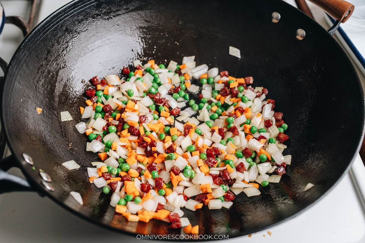 Peas, carrots, onion, and lap cheung stir-fried together in a wok.