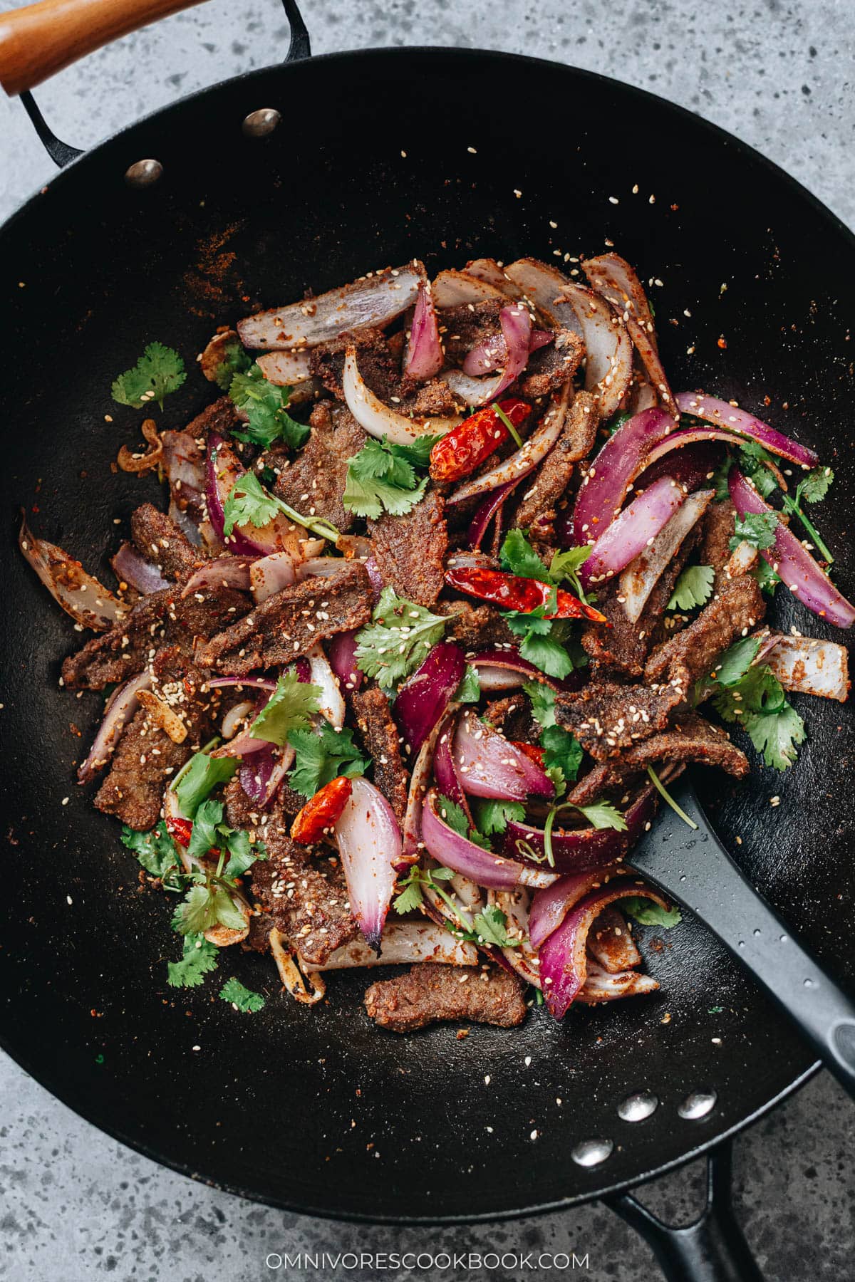 Cumin beef stir-fried with onions, dried chilies, and fresh cilantro in a wok.