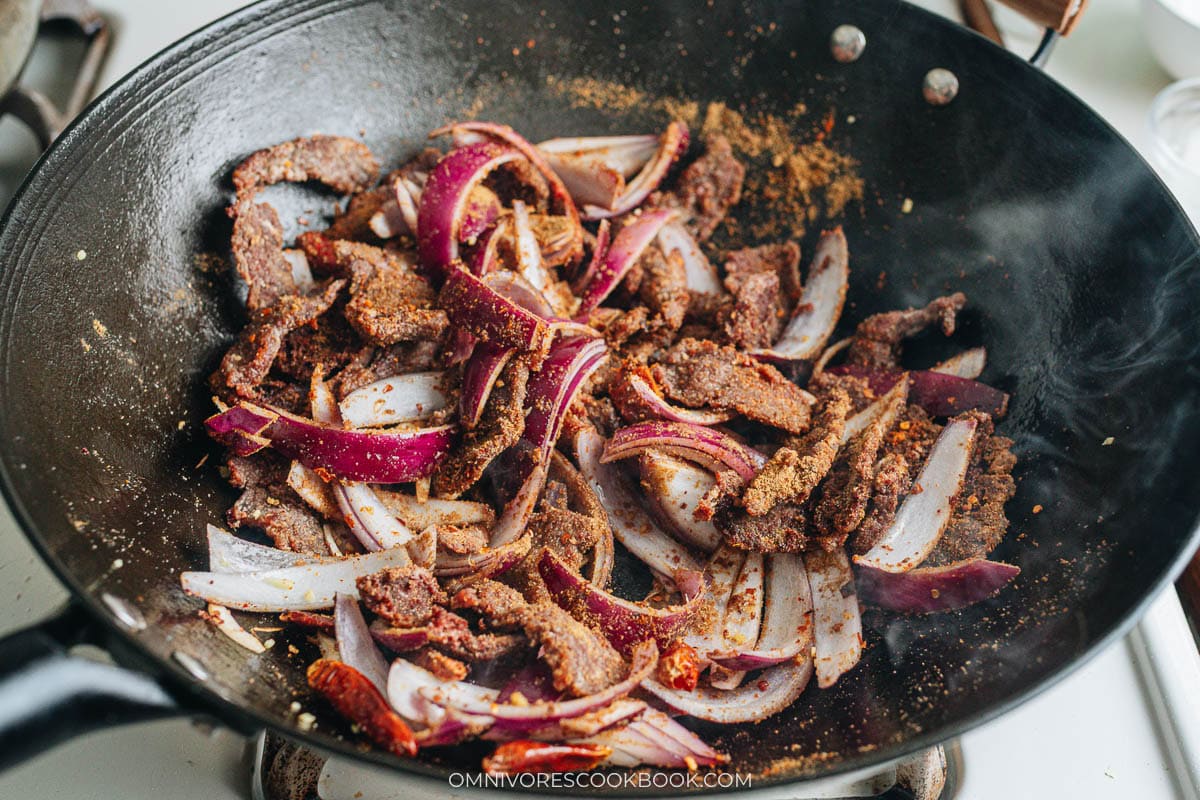 Beef and red onion stir-frying in a wok with cumin spice mix coating the meat.