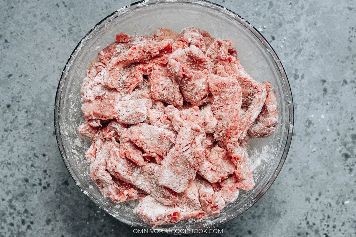 Thinly sliced beef coated in cornstarch and laid out in a bowl, ready for cooking.