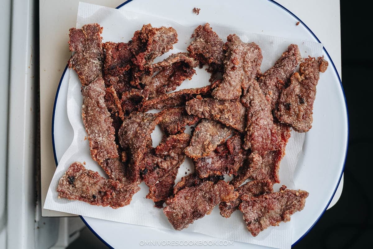Crispy fried beef pieces draining on a paper towel lined plate.